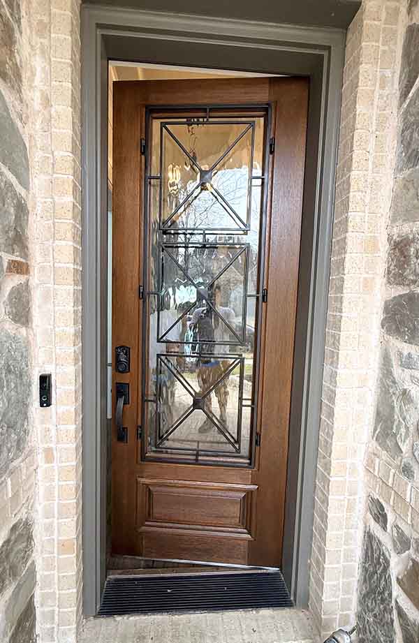 Stained wood front door with decorative glass panels and stone surround in North Dallas home