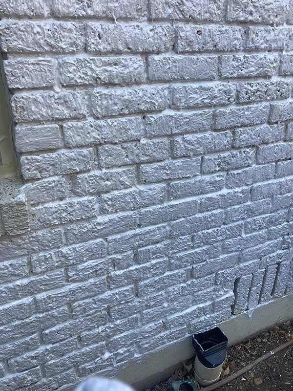 exterior brick wall covered in chemical paint stripper showing thick white gel lifting paint from surface