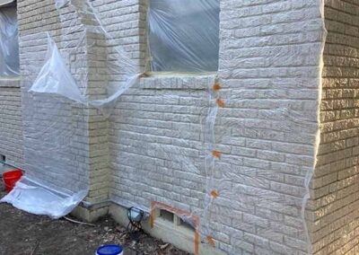 exterior brick corner of home masked with plastic sheeting and tape to protect windows and trim before paint removal