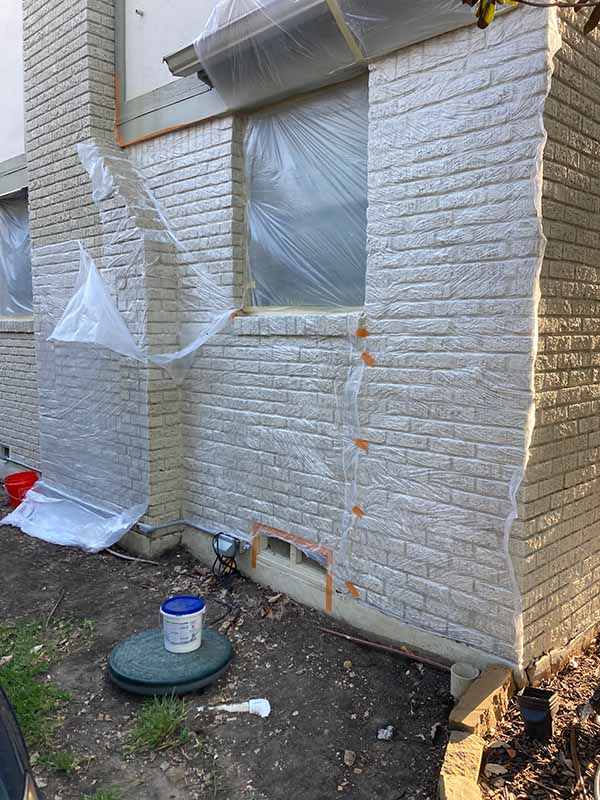 exterior brick corner of home masked with plastic sheeting and tape to protect windows and trim before paint removal