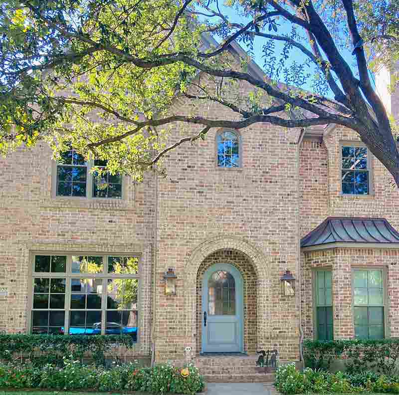 Two-story brick home with painted sage green door, painted trim, and arched entry in North Dallas