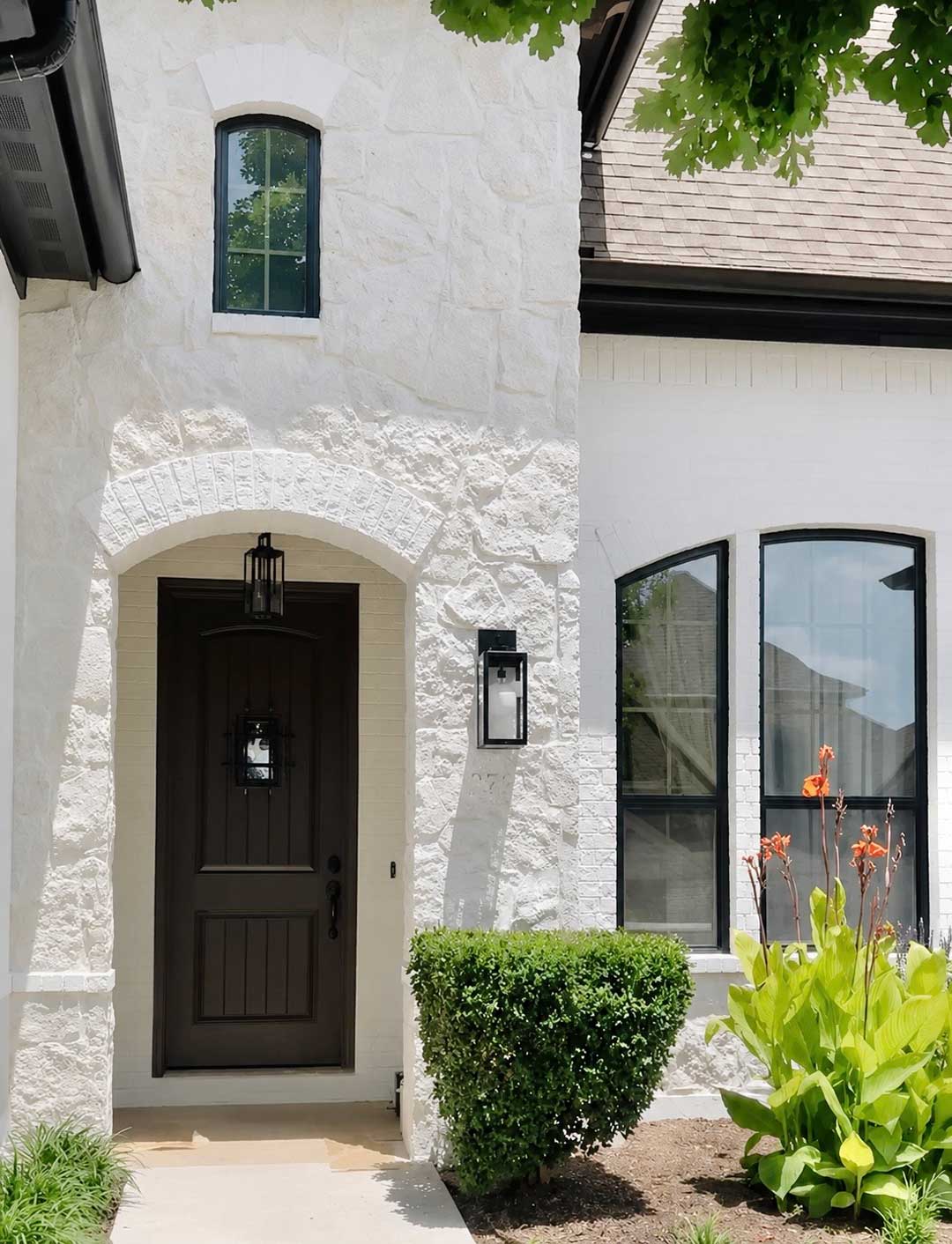 Close-up of painted stone exterior around arched front entry with dark door and black trim detail