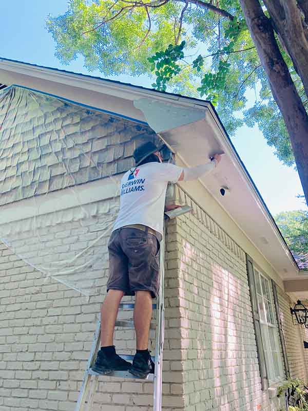 PPP North Dallas painter on ladder painting exterior soffit and trim on brick home