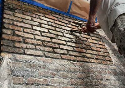 painter hand scrubbing paint from interior brick wall revealing natural brick texture