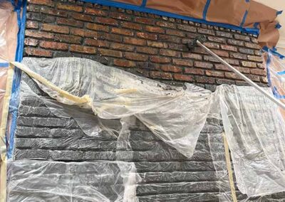 interior brick wall mid paint removal showing restored red brick exposed above covered lower section