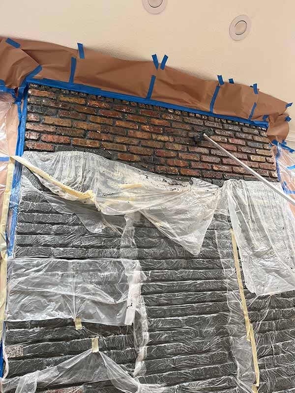 interior brick wall mid paint removal showing restored red brick exposed above covered lower section