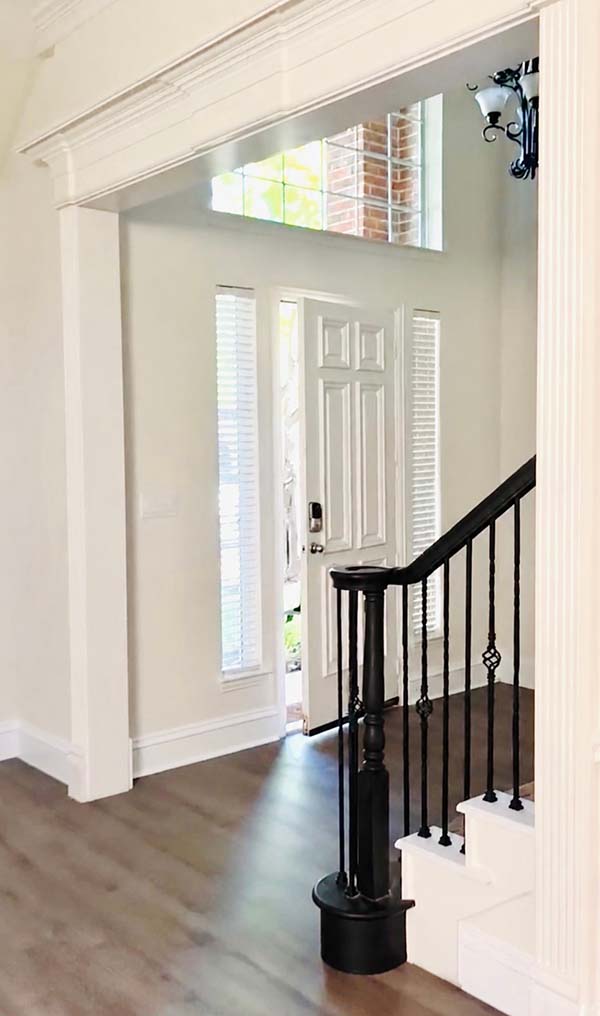 Interior painted white foyer with black painted stair railing and white front door in North Dallas home