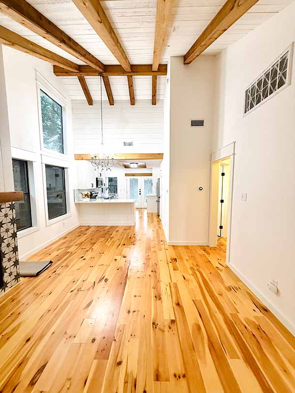 Open interior living space with white shiplap ceiling, wood beams, white walls, and pine hardwood floors in North Dallas
