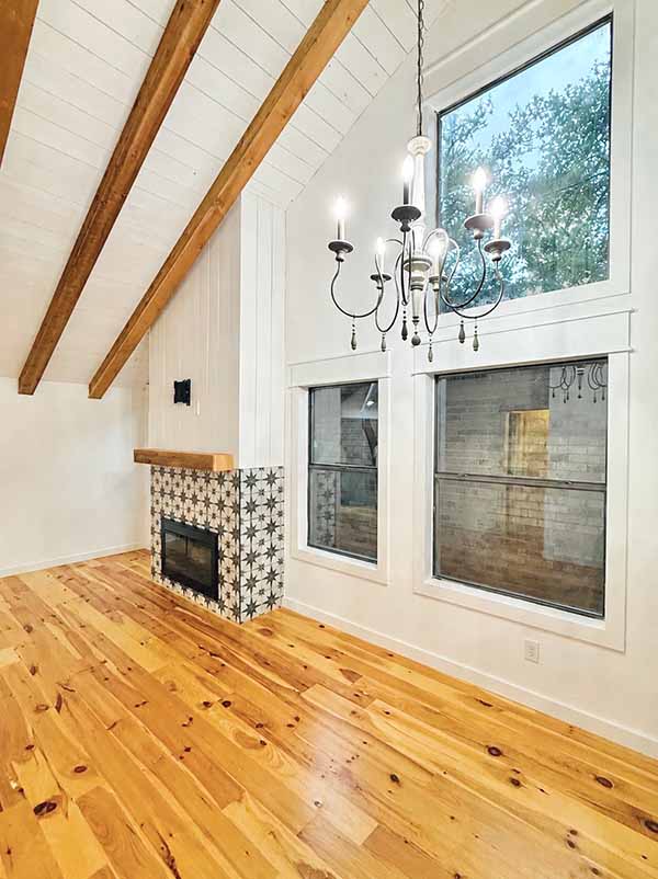 Interior painted white shiplap vaulted room with wood beam ceiling, fireplace, and large windows in North Dallas