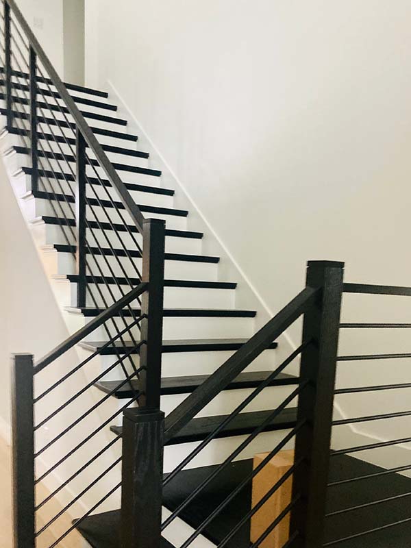 Painted black modern stair railing and treads against white interior walls in North Dallas home