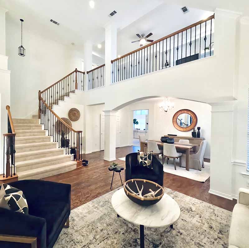 Two-story interior living room with white painted walls, grand staircase, and open floor plan in North Dallas home