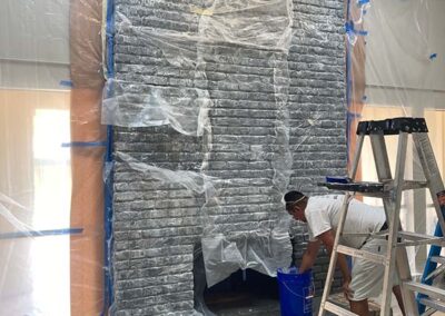 painter preparing interior brick fireplace for paint removal with plastic sheeting and blue tape